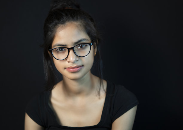 肖像戴眼镜的快乐年轻女子看着相机与牙齿的微笑。图片下载