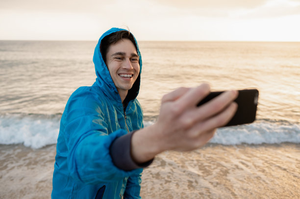 年轻快乐的男性在撒丁岛的海滩上自拍，夕阳西下。图片下载
