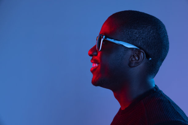 年轻的非洲英俊男子的肖像，摆出孤立的黑色背景在混合霓虹灯。摩天观景轮图片下载