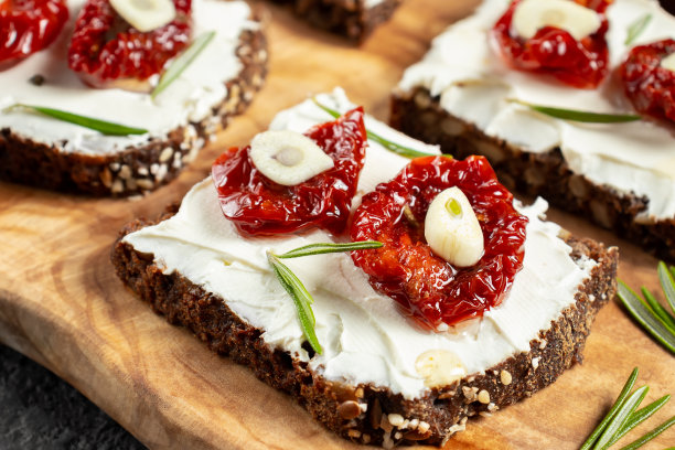 自制杂粮面包三明治，奶油奶酪和晒干的西红柿放在木盘子上，特写。健康饮食的概念图片下载