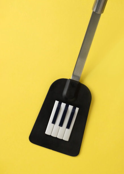 黑色空心匙铲与钢琴键孤立在照亮黄色背景。乐趣、创意、美感、超现实的融合。简约抽象，声学，音乐厨房概念。图片下载