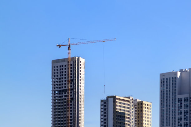 施工起重机和未完工的住宅楼映衬着湛蓝的天空。房屋建设，有脚手架的公寓楼图片下载