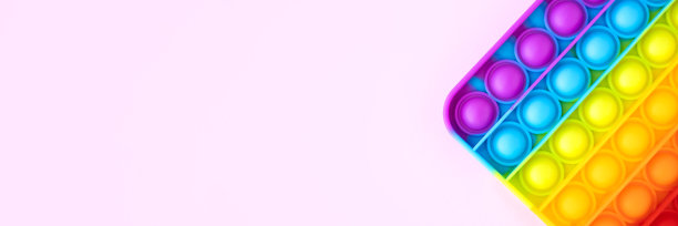 五颜六色的抗压力烦躁推弹它的儿童感官玩具孤立在粉红色的背景与复制空间。简单的酒窝。俯视图，平放。横幅图片下载
