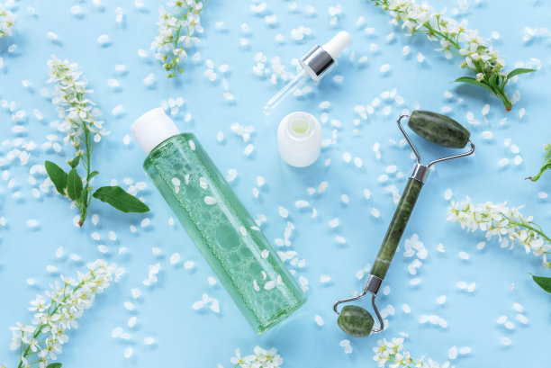 化妆品精华白色无商标瓶，tonik和脸部滚轮。蓝色背景，白色小花和花瓣。俯视图，平放图片下载