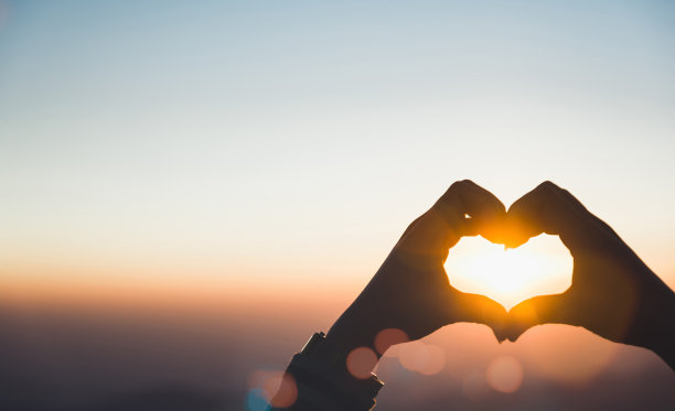 女性的心形手对着天空传递阳光。手形爱心，爱的概念，温暖复古的色调，复制文字空间。图片下载