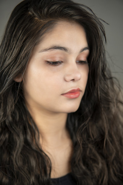 一个美丽的年轻女子的肖像与长卷曲的头发在沉思。图片下载