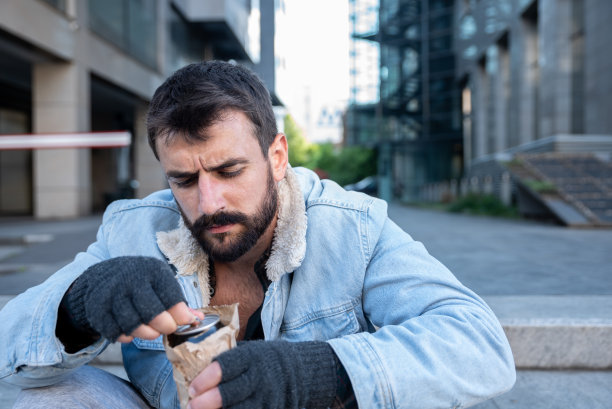 年轻的酒鬼无家可归者坐在街上开啤酒罐藏在纸袋里喝酒，喝醉后被解雇，陷入抑郁，社会纪录片的概念图片下载