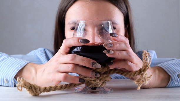 可悲的女人用黄麻绳绑着酒杯。酒精上瘾的概念。酗酒治疗的问题图片下载