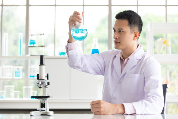 一个年轻的科学家拿着科学玻璃烧瓶和蓝色液体在一个实验室图片下载