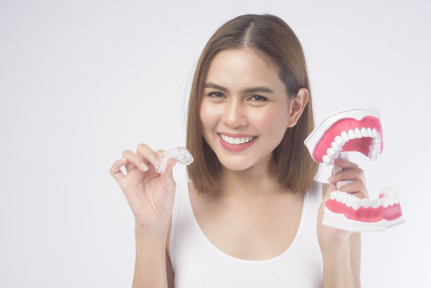 年轻微笑的女人手持无牙矫正器和人工牙科模型在白色背景工作室，牙科保健和正畸概念。图片下载