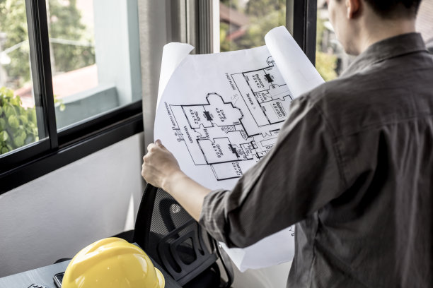 建筑师站在那里，拿着一份房子的设计方案进行检查，他正在与工程师和客户开会，在施工开始前调整设计。楼层平面图和室内设计概念。图片下载