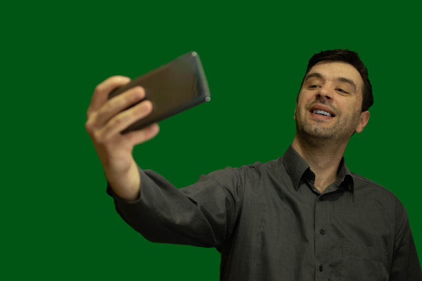 一个年轻人的肖像与绿色的背景，严肃，使用他的手机，愉快的知识分子的人穿着正式的衬衫，戴着太阳镜。图片下载