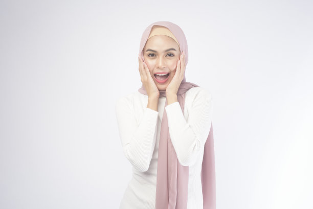 年轻微笑的穆斯林妇女的肖像穿着粉红色的头巾在白色的背景工作室。图片下载