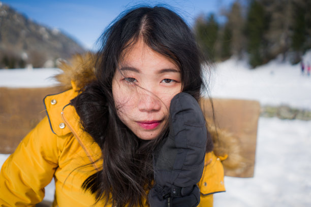 这是一幅年轻、凉爽、迷人的亚洲华裔女子的肖像，她穿着黄色的冬季夹克，在瑞士阿尔卑斯山脉上冰冻的湖面上愉快地微笑着图片下载