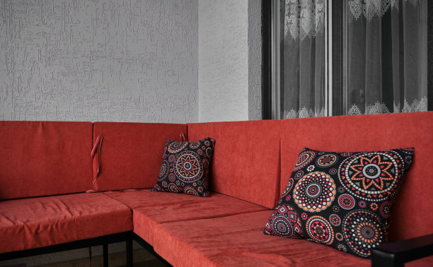 复古风格的沙发与红色的休息区和五颜六色的图案枕头在它与大窗户和灰泥墙背景。图片下载
