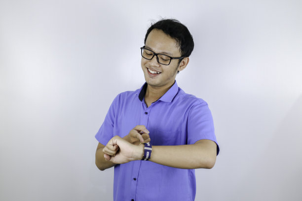 年轻的亚洲男子穿蓝色衬衫是幸福的，并指着看手表孤立在白色的背景图片下载