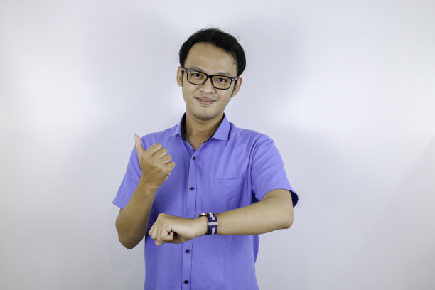年轻的亚洲男子穿蓝色衬衫是幸福的，并指着看手表孤立在白色的背景图片下载