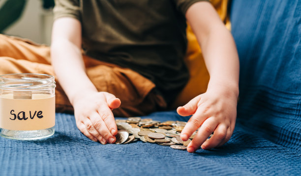 近距离的小男孩的手抓和把堆栈硬币在玻璃罐与保存标签。捐赠、省钱、慈善、家庭理财计划理念图片下载
