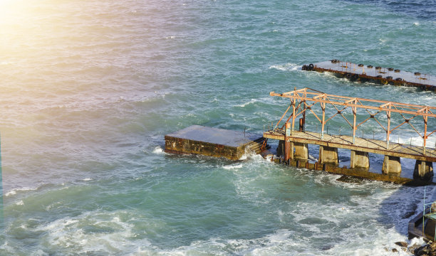 在一个阳光明媚的日子里，蓝色的大海和天空与一个古老的海边码头在一个悬崖上的背景景观图片下载