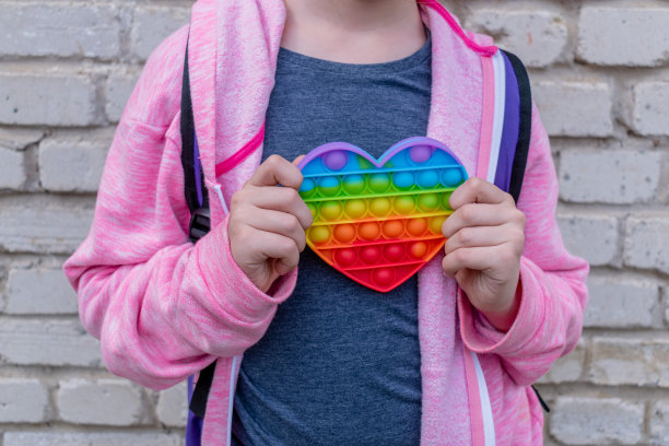 十几岁的女孩拿着pop它形状的心。抗压力玩具概念。彩虹的颜色。图片下载
