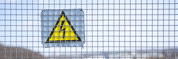 金属网护栏，高压警示标志，警示危险。带闪电的黄色三角形图片下载