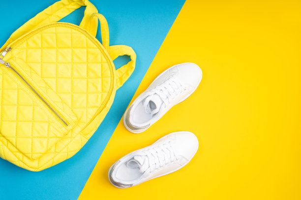 白色的鞋子上有一个黄色的背包，背景是蓝色和黄色，广告照片。白色时尚运动鞋。图片下载