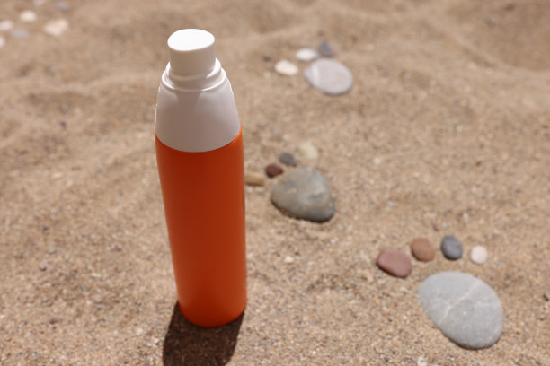 沙子上放着防晒霜，旁边是铺着脚的石头。图片下载