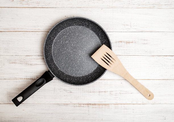 用不粘陶瓷涂层和抹刀在白色木制背景上煎锅。烹饪不粘或油。图片下载