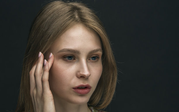 一个头疼的年轻女子在黑暗的背景下揉着她的太阳穴。图片下载