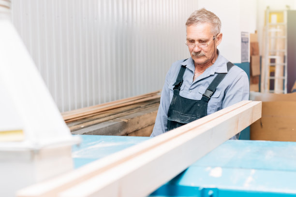 一个年老的木匠或木匠在木匠作坊里用木板工作的肖像图片下载