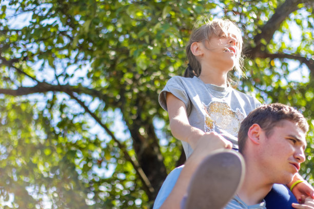 散了焦的哥哥骑在姐姐的背上。快乐女孩的肖像在男人的肩膀上，背着。女孩飞。家人在户外玩耍。绿树模糊的背景。特写镜头。的焦点图片下载