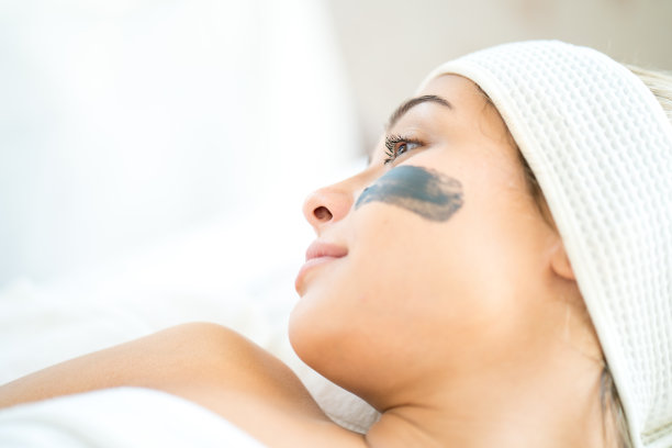水疗中心的工作人员正在把护肤霜涂在脸上。一个年轻女子在水疗沙龙里用面具蒙面。一位年轻的白种女子在美容院按摩。图片下载