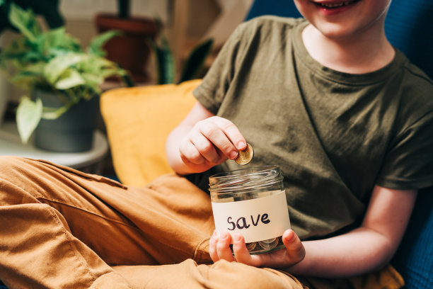 近距离的小男孩的手抓和把堆栈硬币在玻璃罐与保存标签。捐赠、省钱、慈善、家庭理财计划理念图片下载