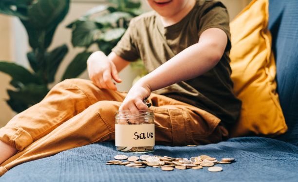近距离的小男孩的手抓和把堆栈硬币在玻璃罐与保存标签。捐赠、省钱、慈善、家庭理财计划理念图片下载