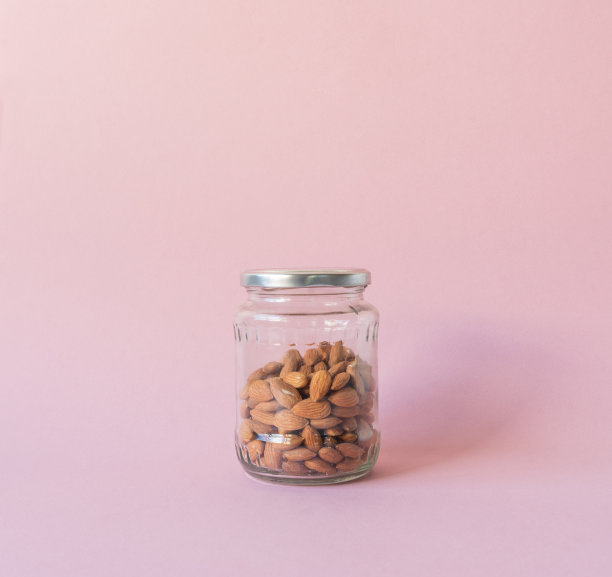 粉红色背景的玻璃罐子里的生杏仁图片下载
