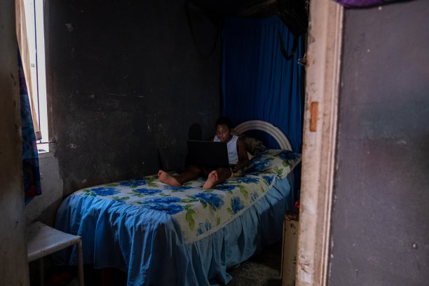 男孩坐在床上用笔记本电脑工作图片下载