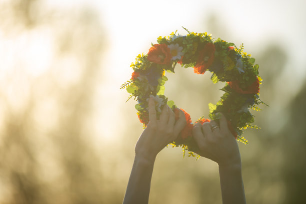 手拿仲夏花的花圈，在夕阳下。古老的拉脱维亚文化传统LIGO。拉脱维亚的仲夏夜庆祝活动。图片下载