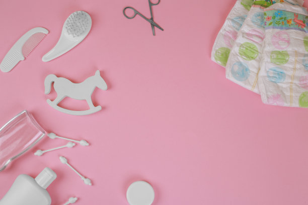 粉红色背景上的婴儿饰品，平铺。组合与婴儿配件和空间的文字。婴儿棉签，剪刀，梳子，油，婴儿拨浪鼓图片下载