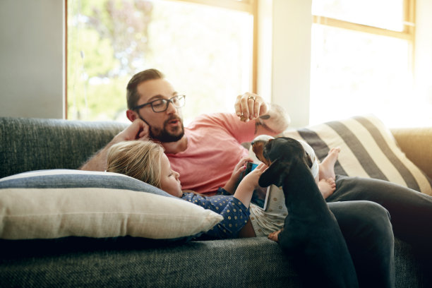 这张照片拍摄的是一位父亲和他的小女儿在家里和他们的狗狗一起使用电子平板电脑图片下载