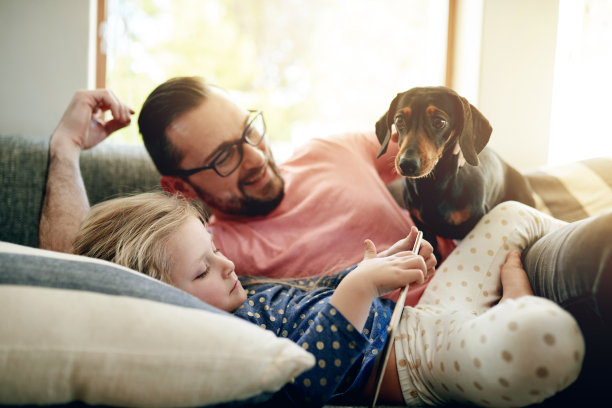 这张照片拍摄的是一位父亲和他的小女儿在家里和他们的狗狗一起使用电子平板电脑图片下载