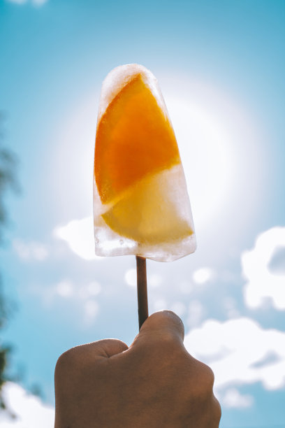 在蓝天的背景下，孩子手中的棒冰。冰淇淋用橙子和柠檬片，垂直排列图片下载