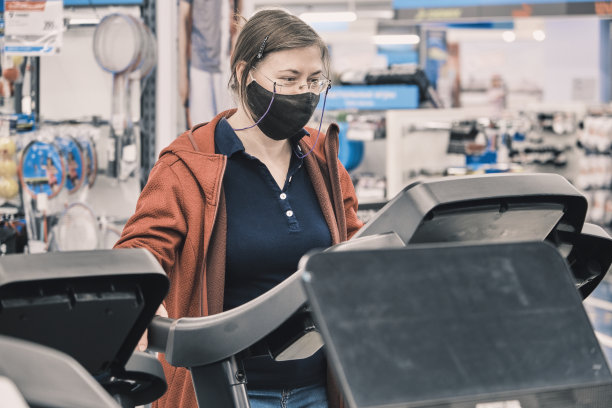 戴着眼镜和防毒面具的严肃女人在商店买了大型跑步机图片下载