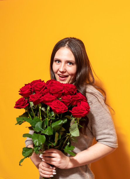 女孩手里拿着一束鲜红的玫瑰，她很惊讶。那张脸模糊不清。黄色背景。有选择性的重点。图片下载