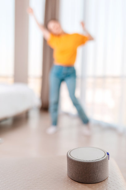 便携式智能扬声器可以播放音乐。背景中，一个女人在一片模糊中跳舞。垂直的。现代小工具的概念图片下载