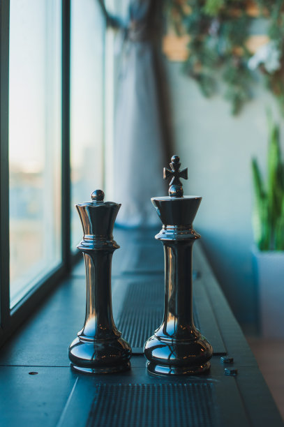 象棋棋子，黑色的国王和王后，大的棋子立在房间靠近窗户的一个黑色窗台上。图片下载