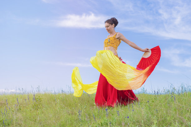 一位身着民族服装的年轻女子，在蓝天的映衬下，在大自然的怀抱中跳着东方舞蹈。户外活动。图片下载