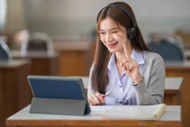 年轻的互动快乐的亚洲少女大学学生学习和展示她的课通过视频在一个数字平板电脑在教室独自一人。教育库存图片图片下载