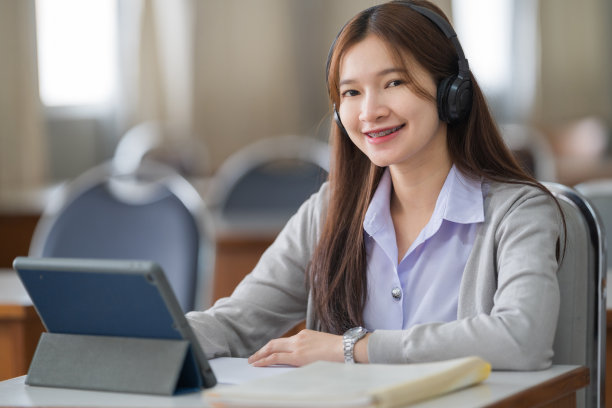 年轻的互动快乐的亚洲少女大学学生学习和展示她的课通过视频在一个数字平板电脑在教室独自一人。教育库存图片图片下载