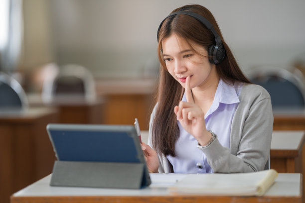 年轻的互动快乐的亚洲少女大学学生学习和展示她的课通过视频在一个数字平板电脑在教室独自一人。教育库存图片图片下载