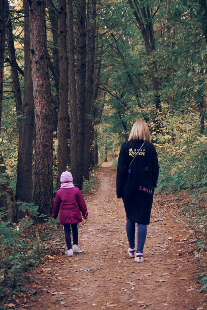 妈妈和女儿手牵着手在公园里散步。队列中人工种植树木。落叶落在地上。家庭母亲和女儿。有选择性的重点。照片模糊了。因设计而失去焦点图片下载
